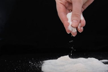 genç bir kadının parmaklarında bir tutam tuz, o tuz bir tepeye aşağı döker. Siyah arka plan daki resim. Konsept - tuzsuz diyet