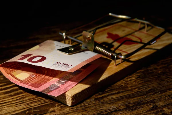 In the wooden mouse trap there is a ten euro bill against a dark background. Concept - risky financial transactions, fraud, risky investments. \