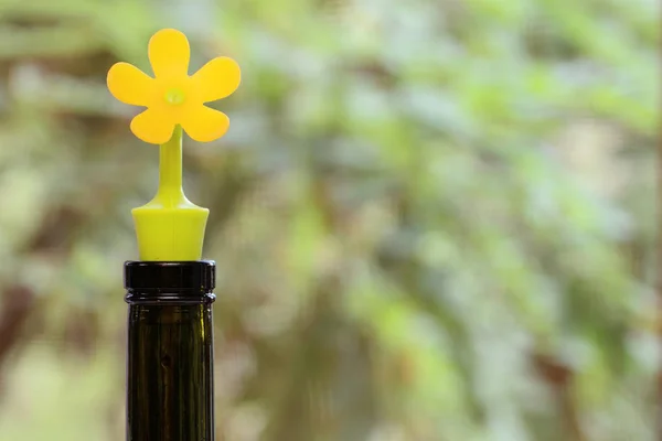 the neck of a wine bottle is plugged with a yellow rubber stopper in the shape of a flower against a blurred background. Concept - sunny wine