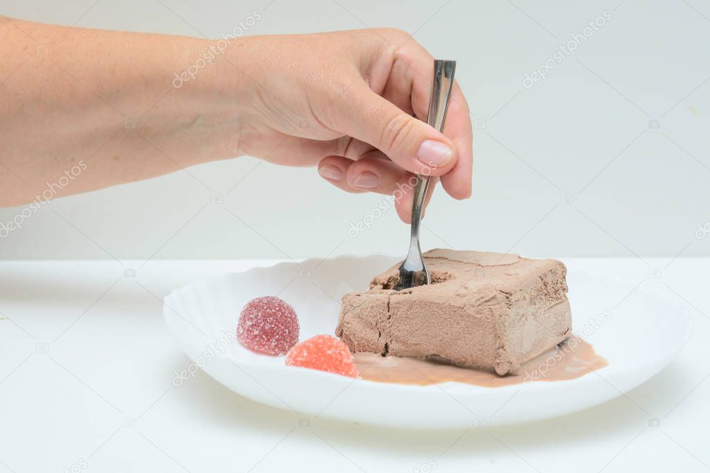 On a white plate is coffee ice cream and two marmalades. In a female hand a teaspoon. A woman is trying ice cream. Concert - dessert