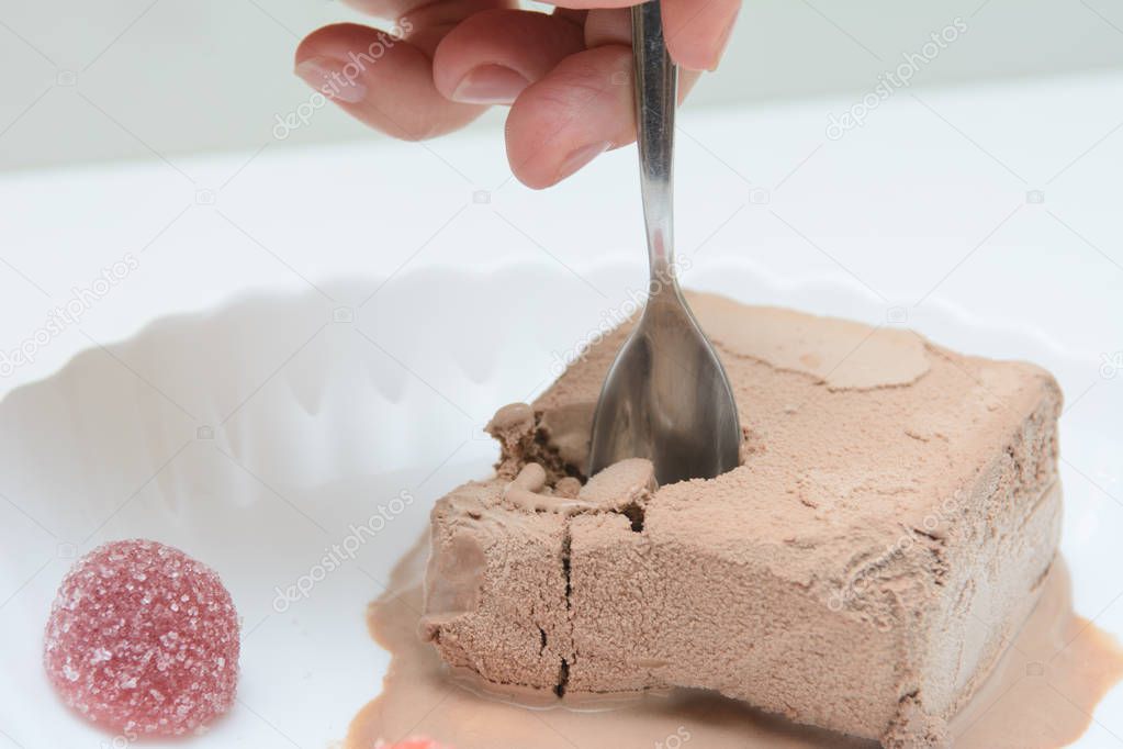 On a white plate is coffee ice cream and two marmalades. In a female hand a teaspoon. A woman is trying ice cream. Concert - dessert