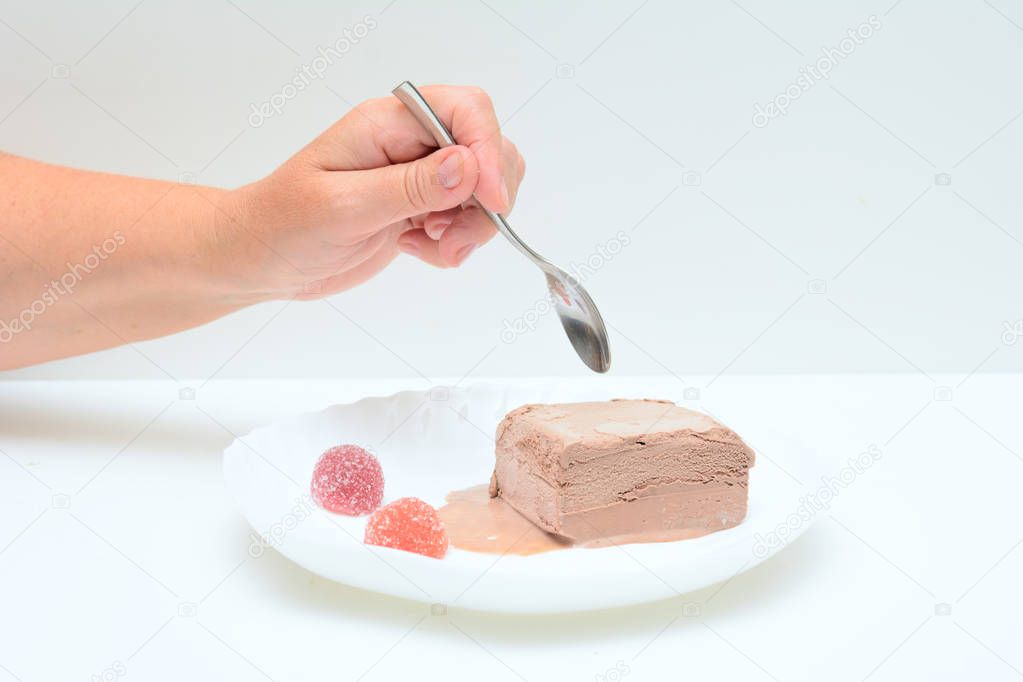On a white plate is coffee ice cream and two marmalades. In a female hand a teaspoon. A woman is trying ice cream. Concert - dessert