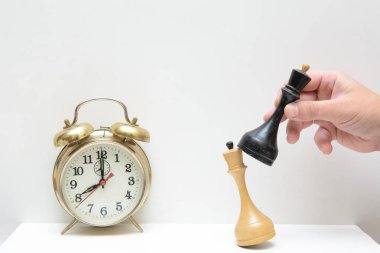 Klasik bir çalar saatin arka planında, siyah satranç kralı olan bir erkek eli beyaz bir satranç kralını devirdi. Konsept jeopolitik çatışmadır. Güneşte bir yer için mücadele