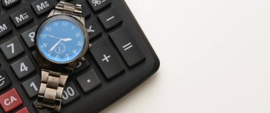 Bir kol saati siyah bir hesap makinesi üzerinde yatıyor. Nesneler beyaz bir arka plan üzerine yerleştirilir. Kavram - bir rapor, muhasebeci, sayma, çalışma zamanı göndermek için zaman.