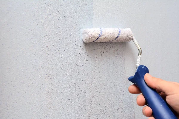 male hand with a roller for painting walls. The painter applies decorative paint to the wall. Concept - repair inside the house