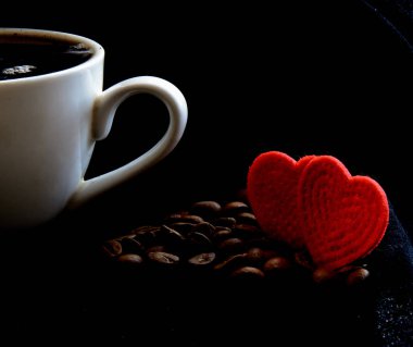 Siyah arka planda kahve fincanı. Kahve çekirdeğinin yanında. İki tane bez kalpleri var. Konsept - Sevgililer Günü sabahı
