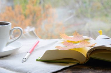 Açık bir kitap beyaz havlunun üzerinde yatıyor. Kitapta sonbahar akçaağaç yaprakları var. Çeşmenin yanında, dolma kalemin yanında. Konsept - eğitim, sonbahar sınavları