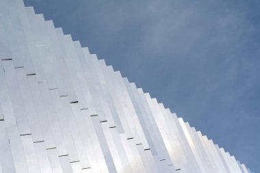 Binanın modern cephesi bulutlu bir gökyüzüne karşı beyaz metalden yapılmıştır. Çapraz görüntü. Kavram-soyut arkaplan