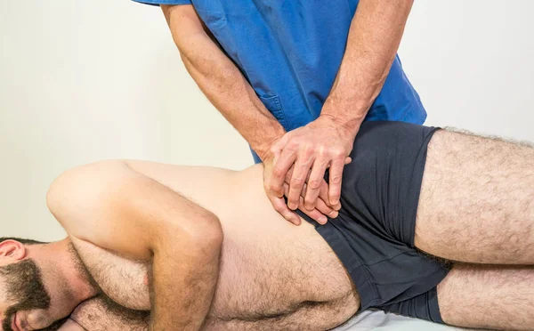 Doktor sjukgymnast bistå en manlig patient samtidigt som man utövar behandling iliaca corection av patienten i en Physio rum, rehabilitering fysioterapikonceptet. — Stockfoto