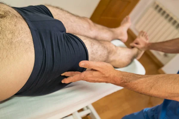 Médico fisioterapeuta assistindo um paciente do sexo masculino, dando exercício rotação do quadril do paciente em uma sala de fisioterapia, conceito de fisioterapia de reabilitação . — Fotografia de Stock
