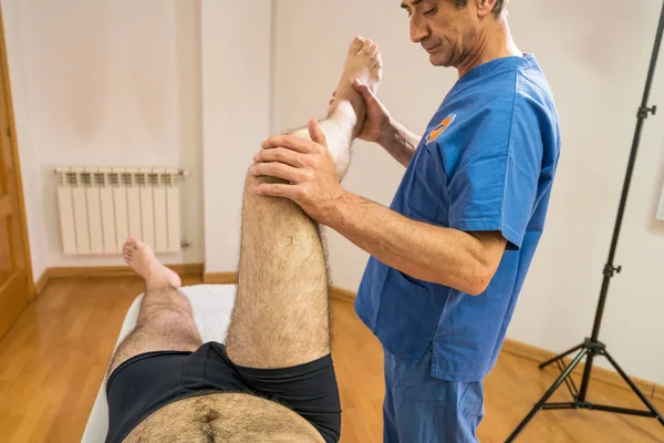Läkare sjukgymnast hjälpa en manlig patient samtidigt som utövar höft av patienten i en Physio rum, rehabilitering fysioterapikonceptet. — Stockfoto