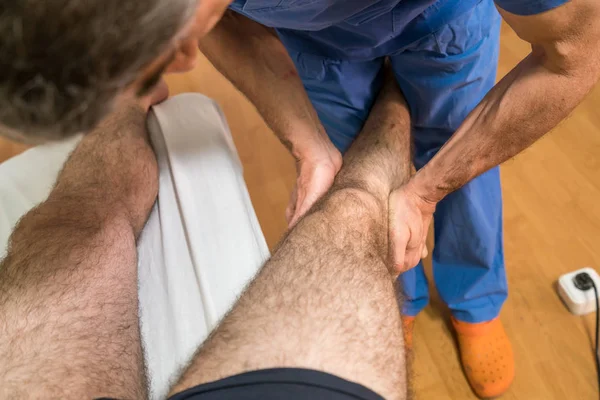 Doktor sjukgymnast hjälpa en manlig patient och samtidigt ge utövar behandling massera till Tibia av patienten i en Physio rum, rehabilitering fysioterapikonceptet.. — Stockfoto