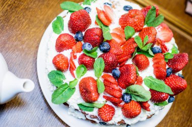 Krem ve nane çilek kek bir plaka masada yaprakları, çay ile bir çaydanlık arka planda, açık renklerde, yakın çekim bulanık bir arka plan ile.