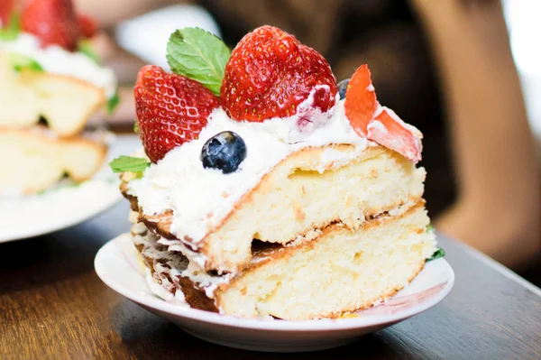 A piece of cake with strawberries in cream, blueberries and mint leaves, on a plate, in light colors close-up