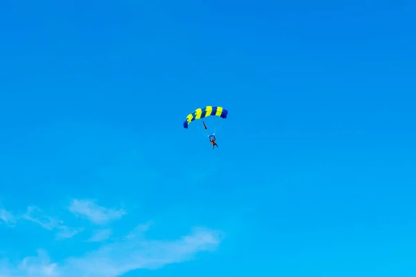 Homem pára-quedista voa sob a asa do paraquedas, descendo e entrando para pousar mais perto do chão em um fundo de céu azul, nuvens brancas — Fotografia de Stock