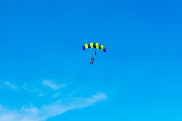 Homem pára-quedista voa sob a asa do paraquedas, descendo e entrando para pousar mais perto do chão em um fundo de céu azul, nuvens brancas — Fotografia de Stock