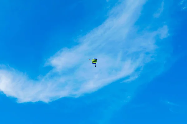 Чоловічий скідайвер летить під крилом парашуту, спускаючись і приходячи на землю ближче до землі на тлі блакитного неба, білих хмар — стокове фото