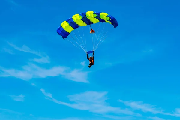 Homem pára-quedista voa sob a asa do paraquedas, descendo e entrando para pousar mais perto do chão em um fundo de céu azul, nuvens brancas — Fotografia de Stock