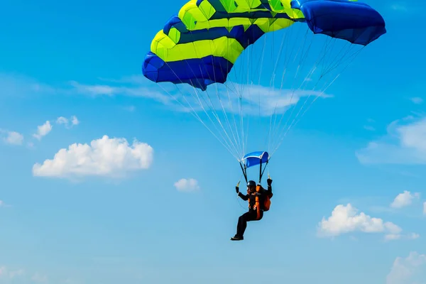 Homem pára-quedista voa sob a asa do paraquedas, descendo e entrando para pousar mais perto do chão em um fundo de céu azul, nuvens brancas — Fotografia de Stock