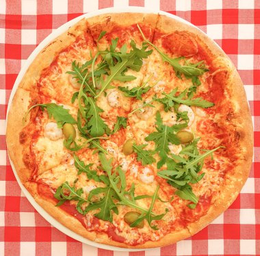 Kırmızı-beyaz damalı masa örtüsü üst görünümü pürüzsüz bir arka plan üzerinde karides, zeytin ve arugula ile taze hazırlanmış pizza. Deniz ürünleri ile İtalyan pizza