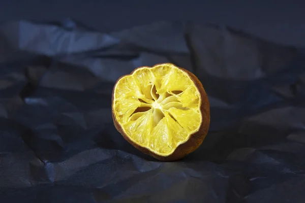 Çirkin organik limon. Zarar görmüş, çürümüş, çirkin kabuklu, büyük kırışıklıkları olan, siyah buruşmuş bir kağıdın üzerinde deforme olmuş bir limon. Yatay oryantasyon. Organik atık
