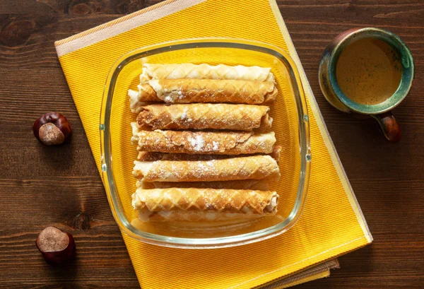Ev yapımı kek. Bir kap bal ve kestane ile koyu kahverengi ahşap arka planda cam kasede pudra şekerli lezzetli waffle tüpleri. Lezzetli tatlı aperatif, üst manzara. Çocuk oyuncağı. Sonbahar havası