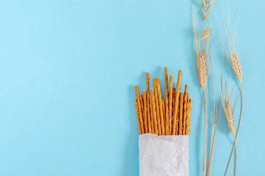 Tuzlu, fırında, beyaz ekolojik kağıttan yapılmış bir çantada buğday çubukları ve mavi arka planda buğday dikenleri.