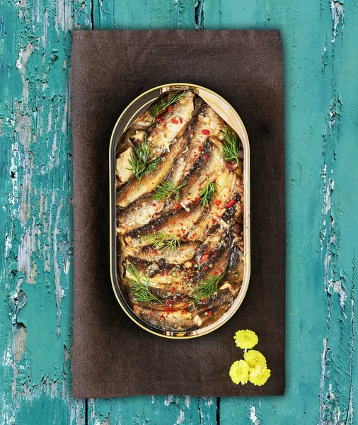 Open tin of Baltic sprats in oil with spices on an old blue wooden background