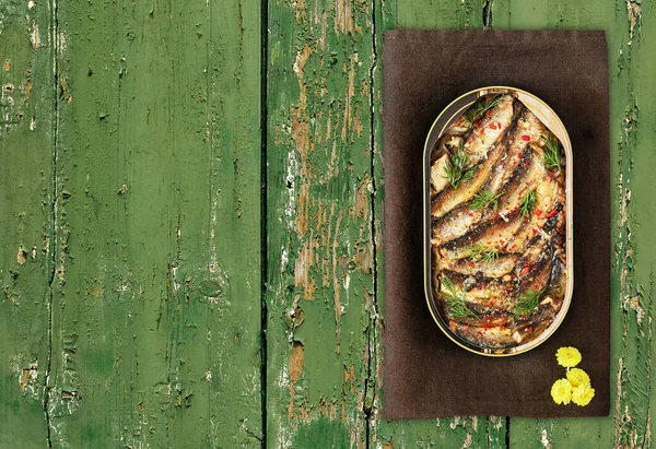 Open tin of Baltic sprats in oil with spices on an old green wooden background