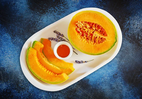 Sweet melon cut into slices with honey and lavender on a white plate — Stock Photo, Image