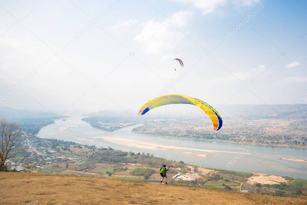 Paragliding in the sky. Paraglider  flying over Landscape from Beautiful View Mekong River at Wat Pha Tak Suea in Nongkhai, Thailand.Aerial view. Concept of extreme sport, taking adventure/ challenge.