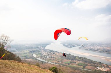Gökyüzünde paraşütle atlıyor. Paraglider, Tayland 'ın Nongkhai kentindeki Wat Pha Tak Suea' daki Güzel Görüş Mekong Nehri 'nden manzara üzerinde uçuyor. Ekstrem spor kavramı, macera / meydan okuma.