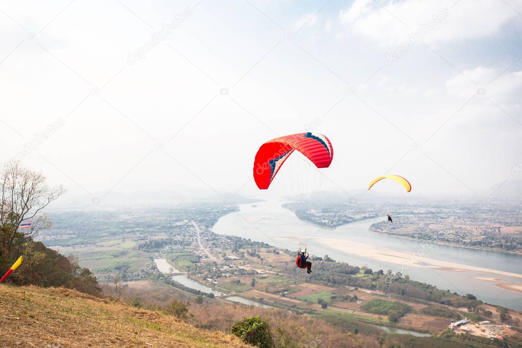 Paragliding in the sky. Paraglider  flying over Landscape from Beautiful View Mekong River at Wat Pha Tak Suea in Nongkhai, Thailand.Aerial view. Concept of extreme sport, taking adventure/ challenge.
