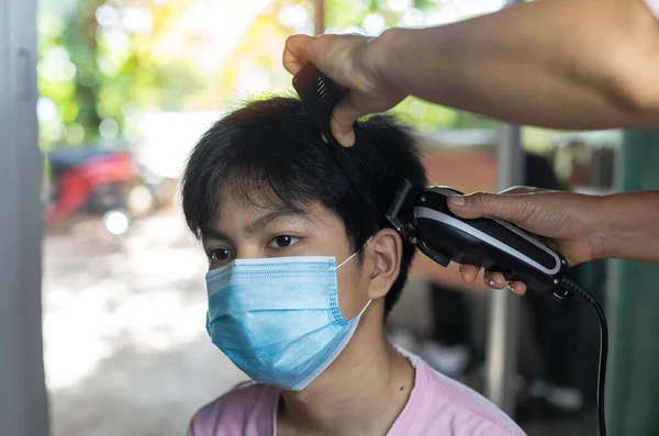 Thai boy in mask getting hair cut in beauty saloon with proper safety measures for Covid-19. Cutting hair of a man in mask. Hair care during Covid-19.Beauty saloons opens after lock down.