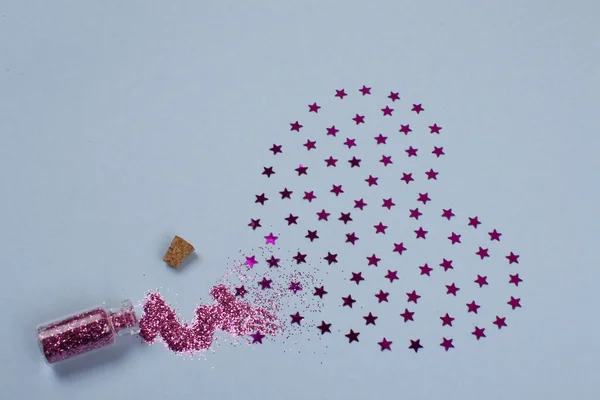 Mavi bir arka plan üzerinde cam kavanozdan düştü pembe payetler pembe kalp.