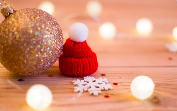 Altın Noel top ve beyaz kar tanesi yanında kırmızı kap. Çelenk ışık onları çevreleyen. Tüm bu ahşap bir arka plan üzerinde.