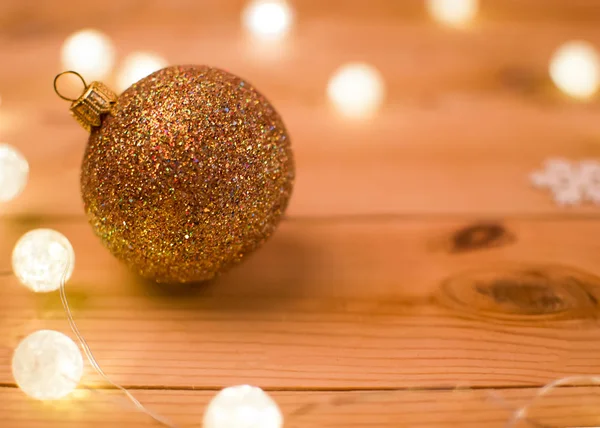 Garland ışıklar tarafından çevrili bir ahşap zemin üzerine altın Noel top.