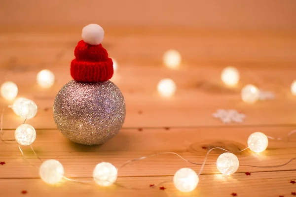 Gümüş Noel top çelenk ışık tarafından çevrili bir ahşap zemin üzerine kırmızı bere ile.