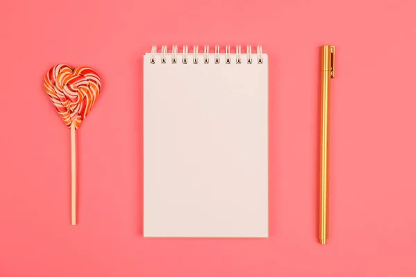 Pembe bir arka plan üzerinde altın kalem ve lolipop kalp ile not etmek.