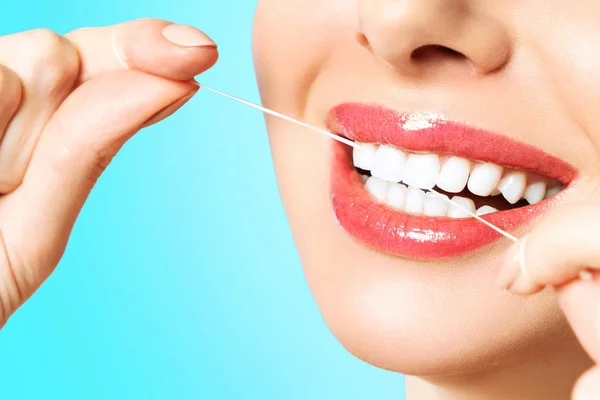 Jonge mooie vrouw is bezig met het schoonmaken van tanden. Mooie glimlach gezonde witte tanden. Een meisje houdt een tand Floss. Het concept van mondhygiëne. — Stockfoto