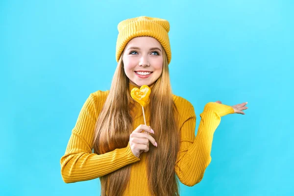 Portrait of a cute girl with a heart shaped lollipop. Sends blows a kiss while looking at the camera, Sexy female lips. Separate on a blue background. — 스톡 사진