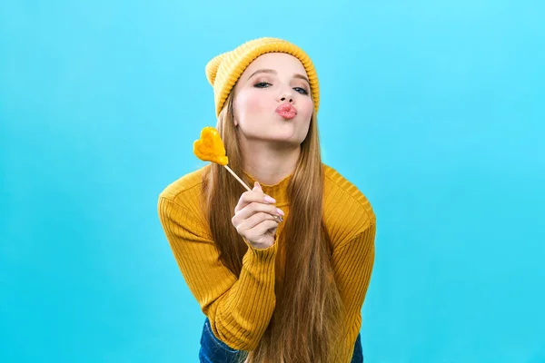 Portrait of a cute girl with a heart shaped lollipop. Sends blows a kiss while looking at the camera, Sexy female lips. Separate on a blue background. — 스톡 사진