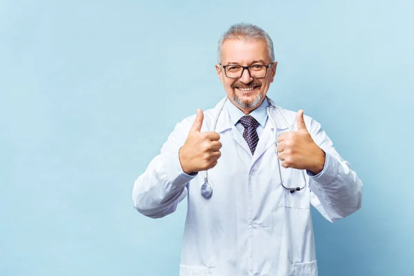 Smiling medical senior doctor with a stethoscope. On a blue background. Medic shows thumb raised up. The concept of humanitys victory over disease