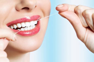 Genç güzel kadın diş temizliği yapan. Güzel gülümseme sağlıklı beyaz dişler. Bir kız diş ipi tutar. Ağız hijyeni kavramı. Bir diş kliniği için promosyonel görüntü