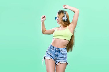 Çok güzel kız eğleniyor ve renkli arka plan üzerinde smartphone kulaklıktan müzik dinler.