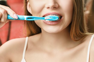 Genç bir kadın banyoda dişlerini fırçalıyor. Aynadaki yansıma.