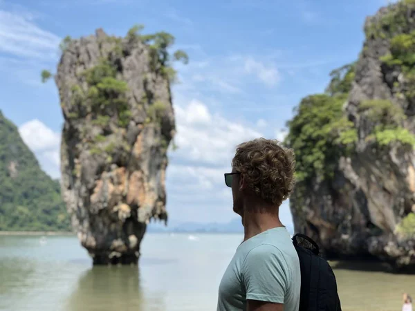 a light-skinned guy in sunglasses and a t-shirt shows his fingers the sign perfectly on the famous James bond island in Thailand, the azure sea and the wonder Islands in the afternoon