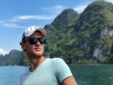 açık tenli adam sarı şapka ve gözlük gülümsüyor ve başarı ve mutluluk zemin bir açık deniz ve uzak Adaları olarak sızar, mavi gökyüzü, bulutlar.