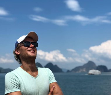 açık tenli adam sarı şapka ve gözlük gülümsüyor ve başarı ve mutluluk zemin bir açık deniz ve uzak Adaları olarak sızar, mavi gökyüzü, bulutlar.