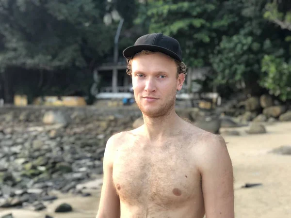 light-skinned blond guy in a cap on the beach without a tan without outerwear smiles